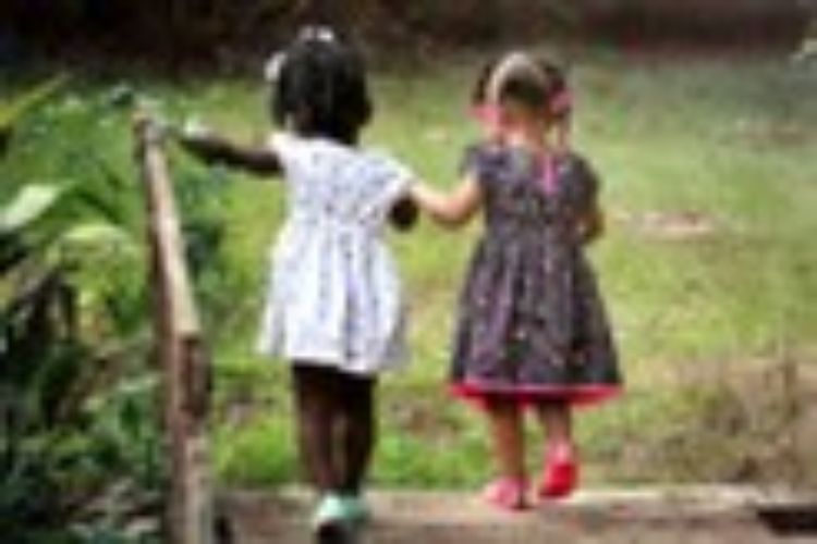 Two little girls in dresses holding hands and walking.