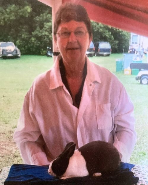 A woman in a white jacket standing behind a black and white rabbit.
