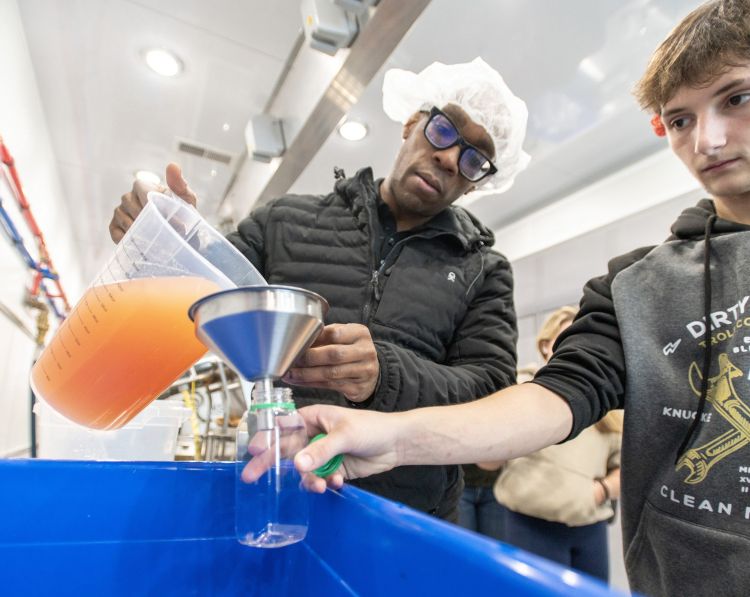 An instructor guides a student as they funnel processed liquid into a bottle during a hands-on training session inside Michigan State University’s mobile food processing lab.