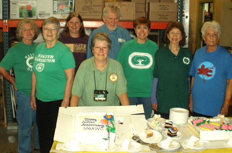 eight people standing in front of a table holding a cake