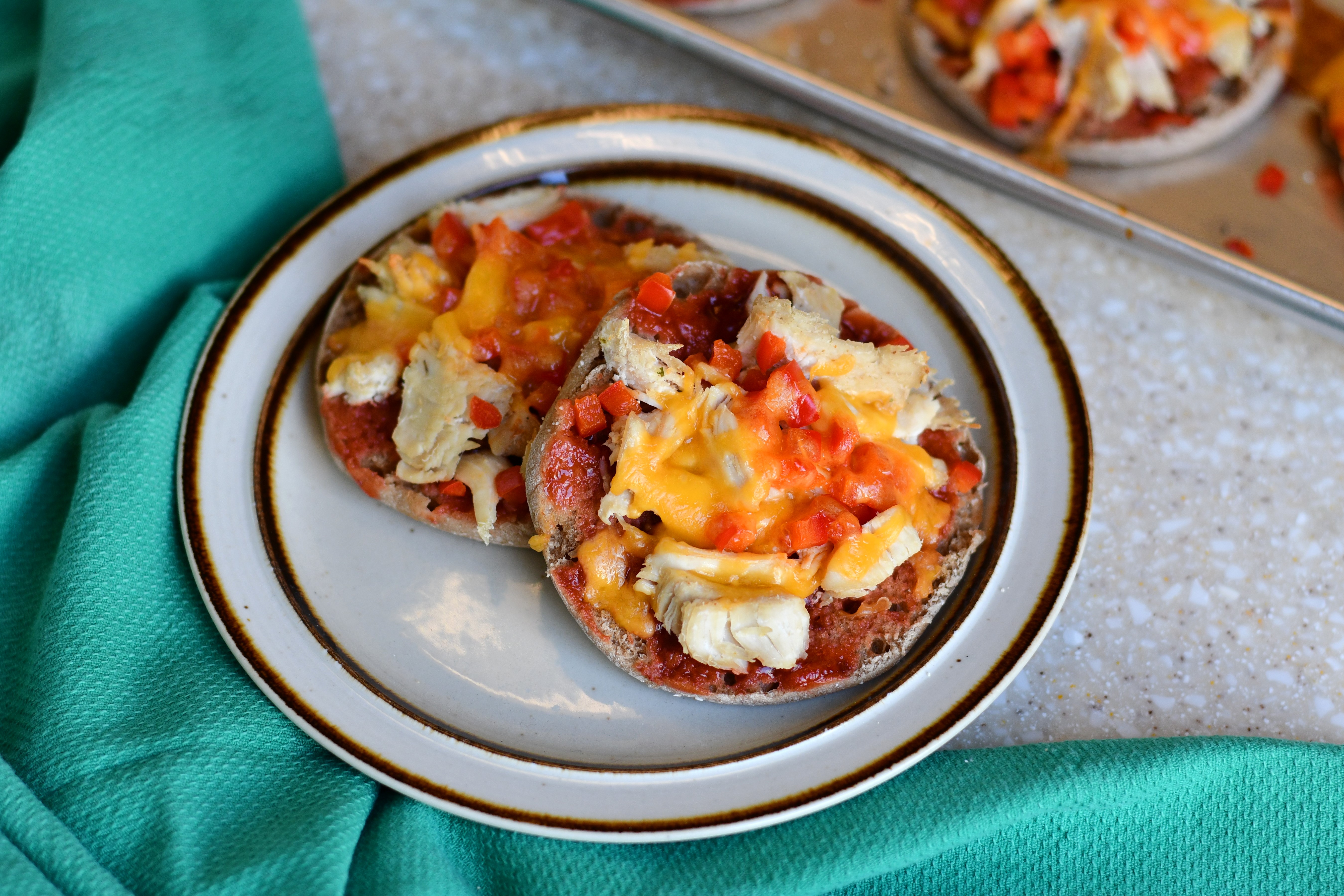 A photo of a plate of mini pizzas with melted cheese and red pepper on a table