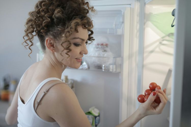A woman looking at produce in front of her fridge.