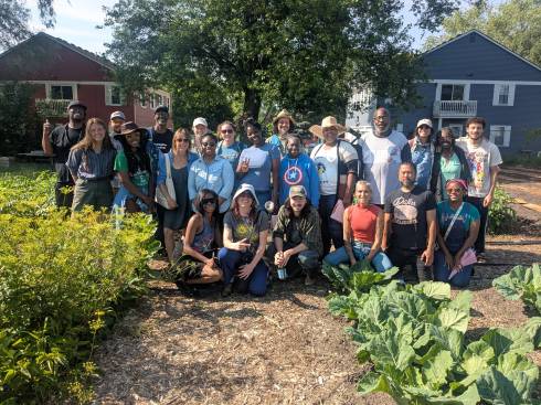 About 25 people pose for a picture in a garden with apartment buildings in the background.