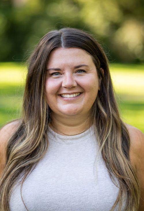 A headshot of Ashley Lathrop smiling with a blurred background outdoors