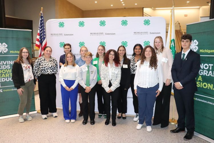 A group of youth dressed up and standing in front of 4-H banners and flags.
