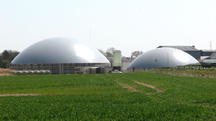 two silver anerobic digester domes in a green field