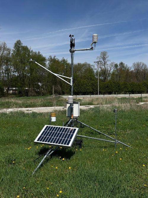 An MSU Enviroweather station in a field near a row of trees.