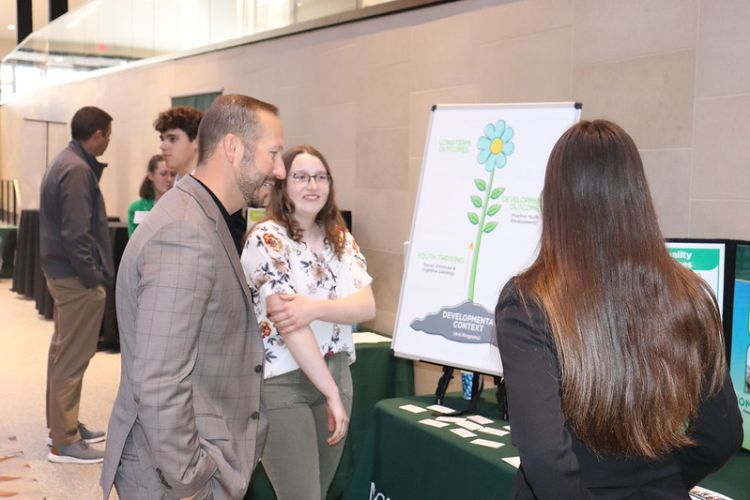 Two young ladies talking to a man in a suite next to a display.
