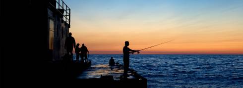Person fishing off a pier at sunset on Lake Michigan. Water is blue and sky is gradients from orange to blue.