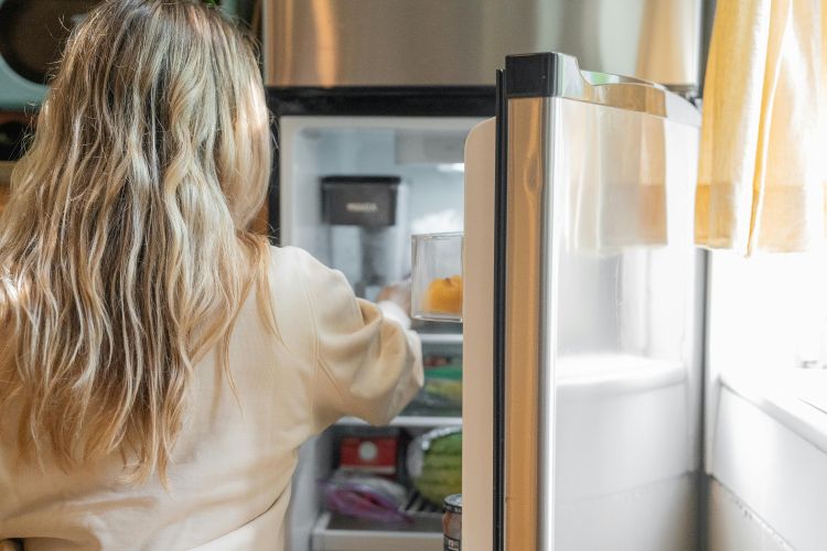 A woman examines food in her refrigerator.