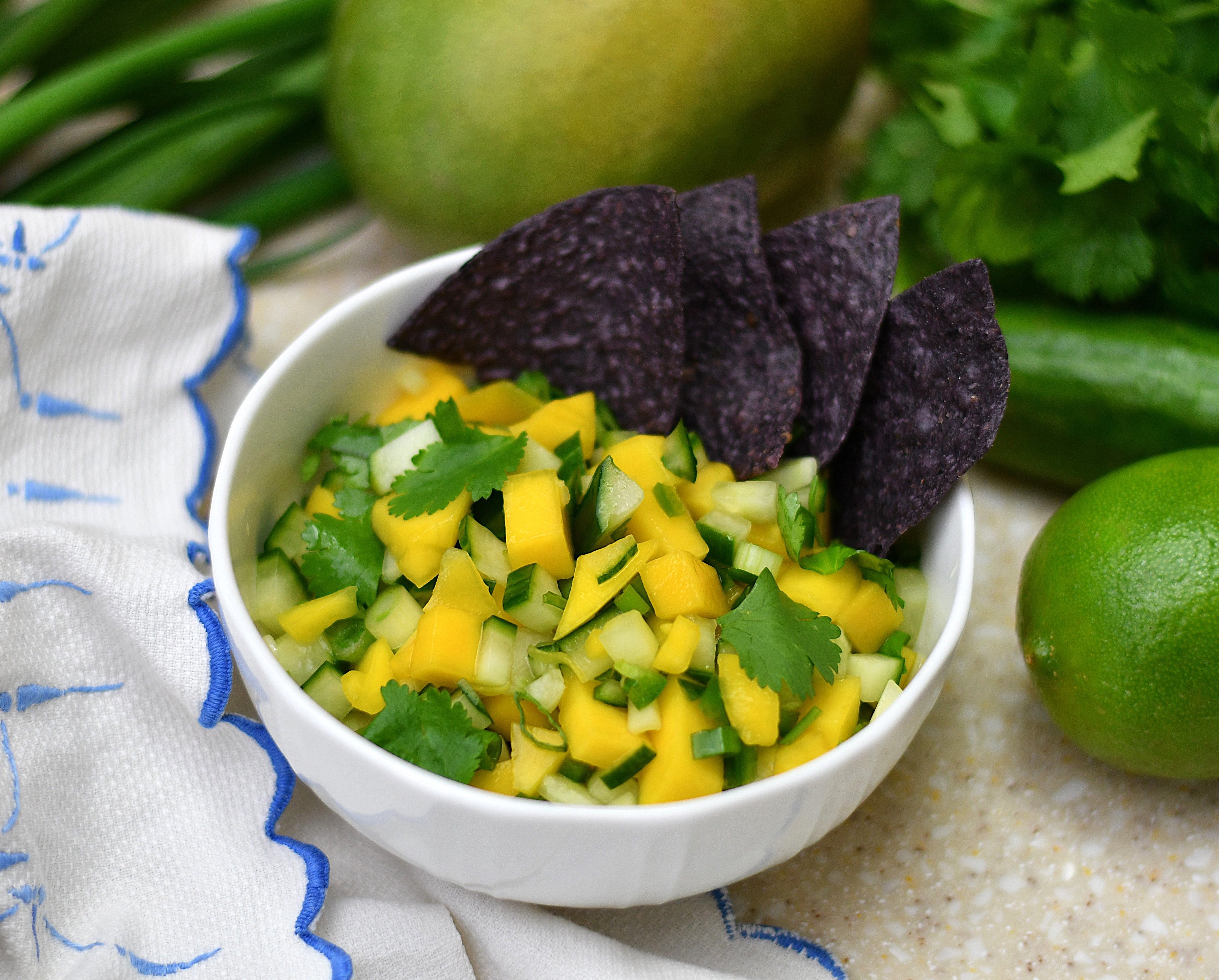 A photo of a bowl of salsa with blue chips next to limes.
