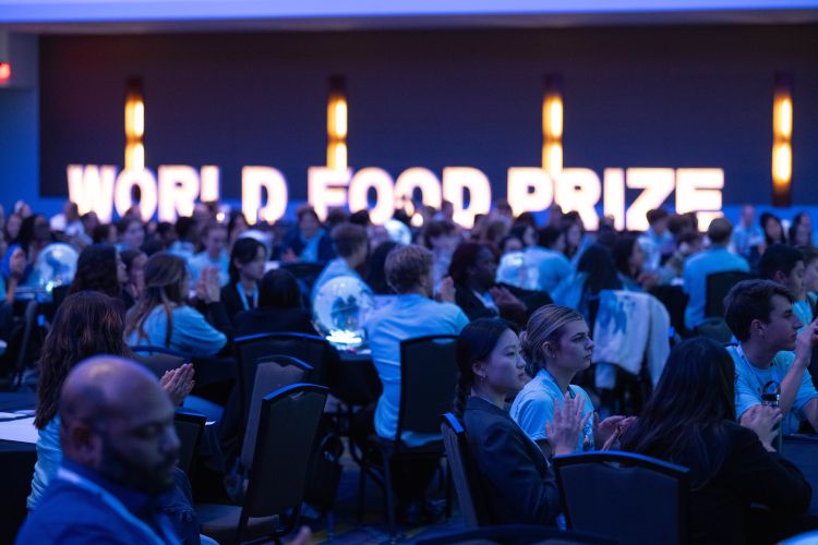 Individuals seated around a dimly lit room. The words World Food Prize are in the distance.