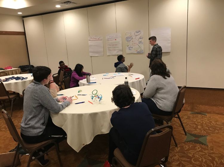 Youth sitting around a table writing ideas on large pieces of paper.