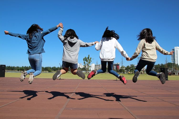 Four girls holding hands and jumping in the air.