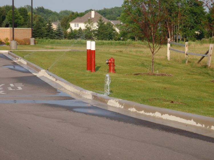 A broken sprinkler floods a parking lot.