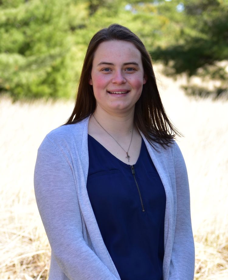 A young white woman with dark hair in a blue shirt and grey cardigan.