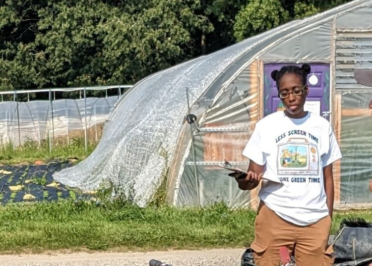 A person with a clipboard standing in front of a hoophouse.