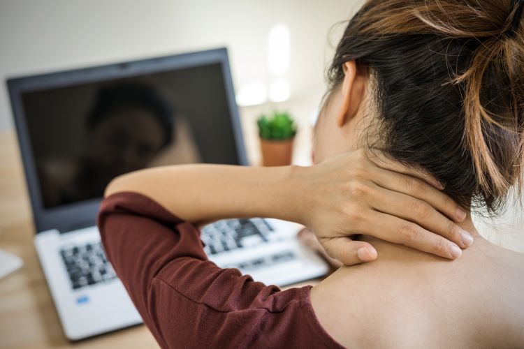 A woman holds her neck while looking at a computer screen.