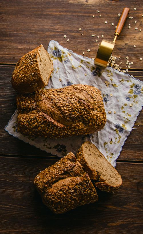 A photo of a cut loaf of bread on a wooden table with oat seeds.