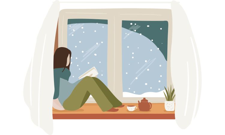 Image of woman reading a book while seated on a windowsill with snow falling outside.