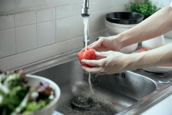 A photo of a person washing an apple under running water in a sink