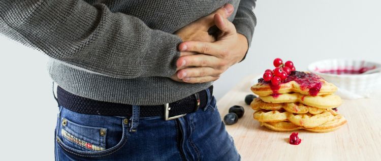 A man holds his stomach in pain, and there is a stack of waffles on the table behind him.
