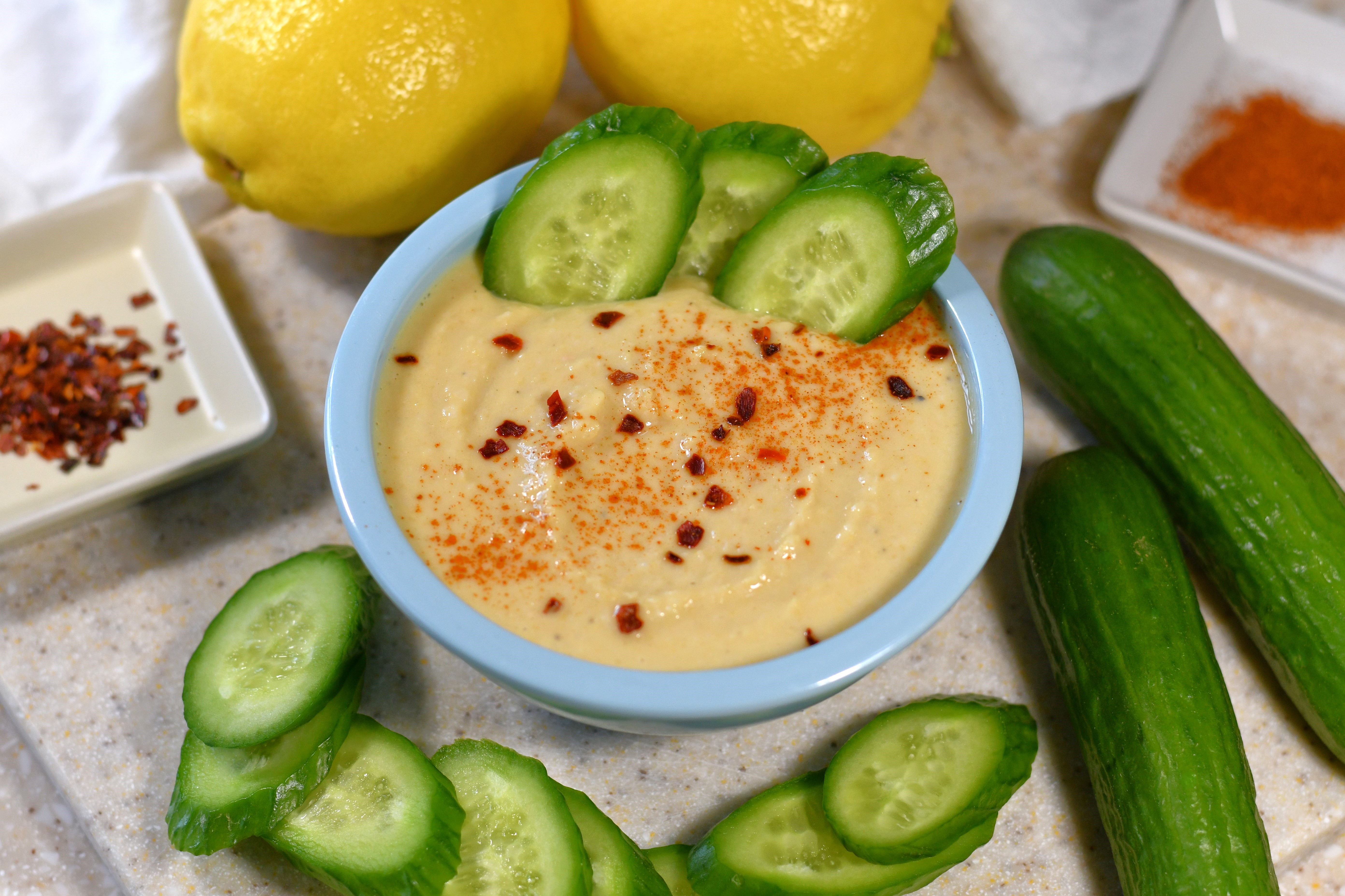 A photo of a bowl of hummus with cucumber slices
