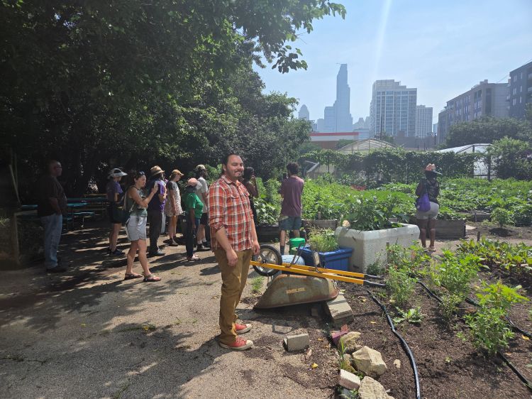 Group of people touring an urban farm in Chicago, with raised garden beds, plants, and city skyscrapers in the background.