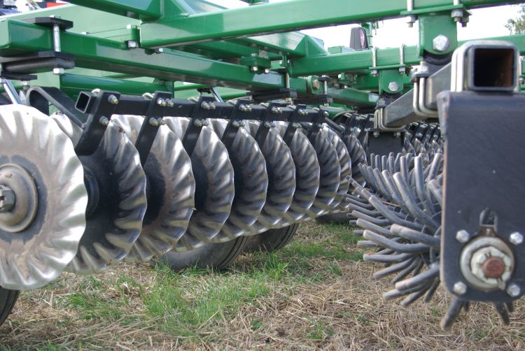 Closeup of vertical coulters on a tillage implement, designed to cut and size crop residue, with a rolling harrow behind to level the seedbed and distribute residue evenly.