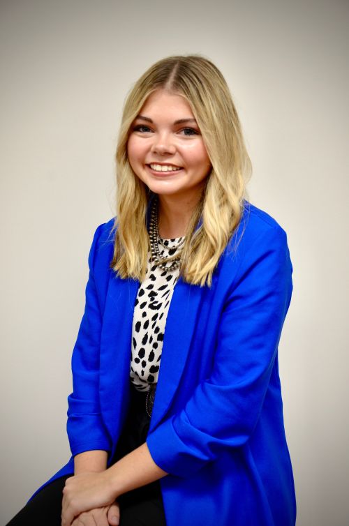 A young blonde girl in a blue blazer and black and white spotted shirt.