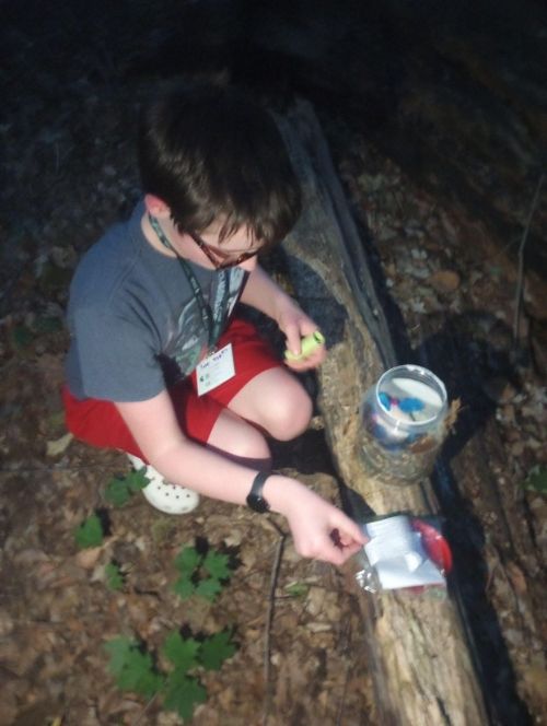 a teenager finding a geocache in Sanford Natural Area outside of Holmes Hall at MSU.