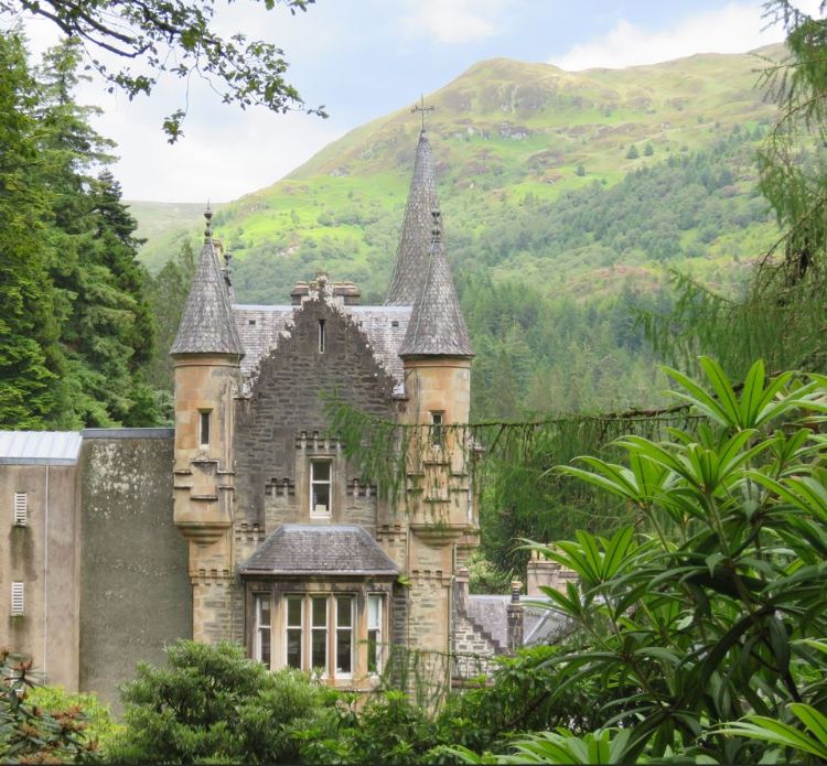 A castle in Scottland surrounded by gardens and trees and mountains.