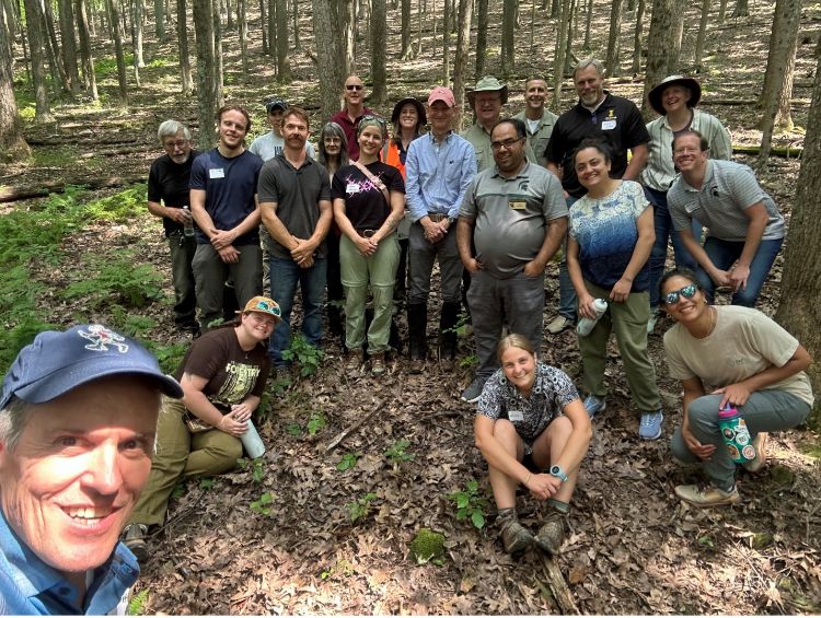 Workshop attendees pose for a picture in a wooded forest.
