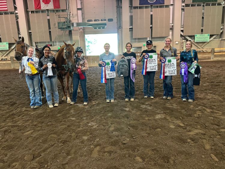 A group of young people holding up ribbons next to horses.