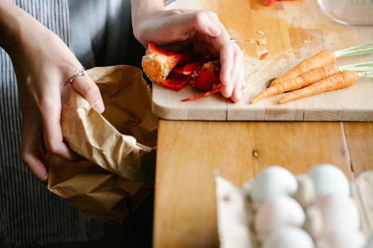 A person scrapes food waste into a paper bag.