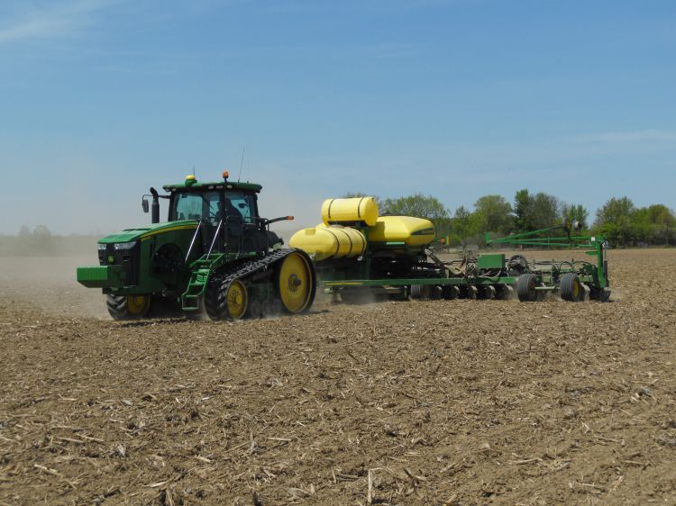 planting soybeans on a brown field with a green tractor and a yellow and green planter