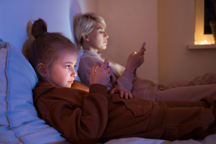 A parent and child looking at phone screens in the dark before going to bed.