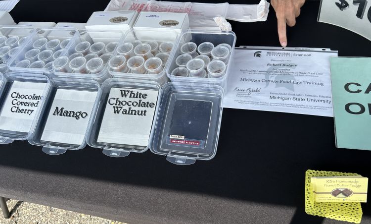 A man pointing at his Cottage Food Law training certificate on a farmers market table.