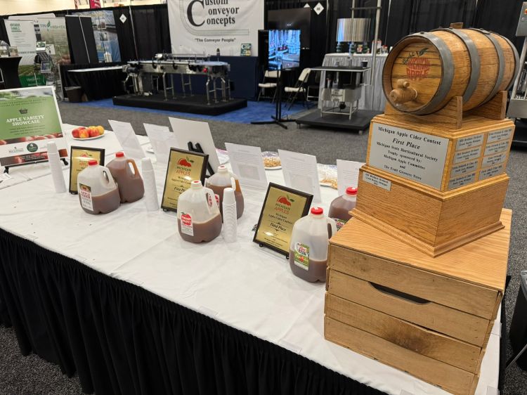 Award-winning gallons of cider sit on a table next to plaques and a large trophy.