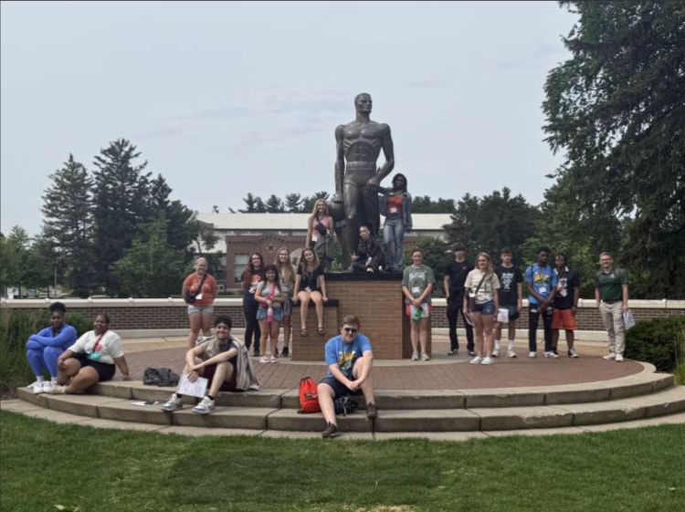 A group of youth standing and sitting around the Sparty statue on the campus of MSU.