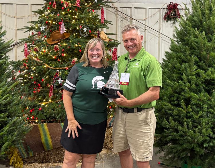 Terri and Bert Cregg pose for a picture in front of Christmas trees while holding an award.