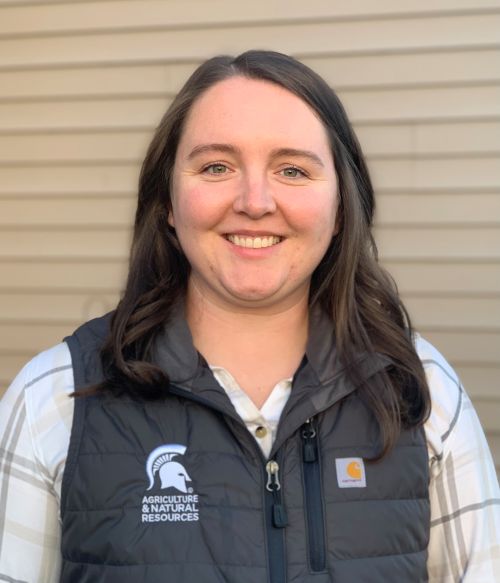 A headshot of Lynn Worden smiling, wearing a black vest with a Spartan helmet on the front