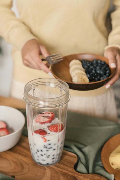 Photo of a smoothie being made that contains berries, milk, and bananas.
