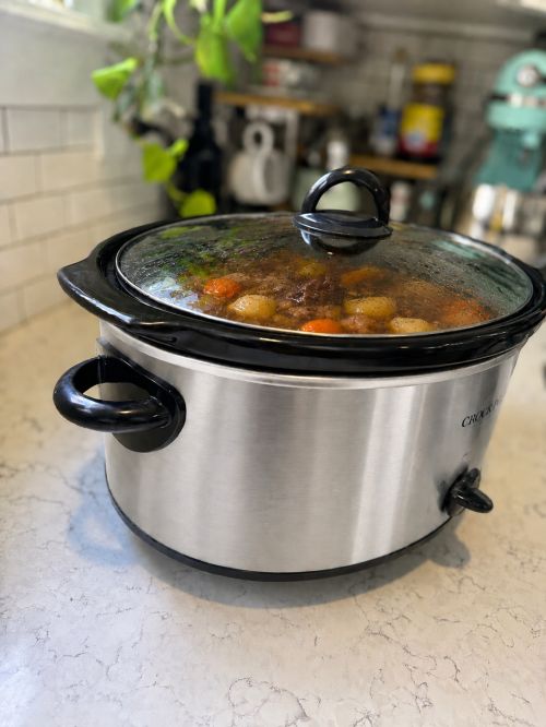 A slow cooker filled with beef stew cooking inside it.