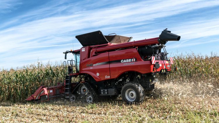 red harvester harvesting green and brown corn with a blue sky background