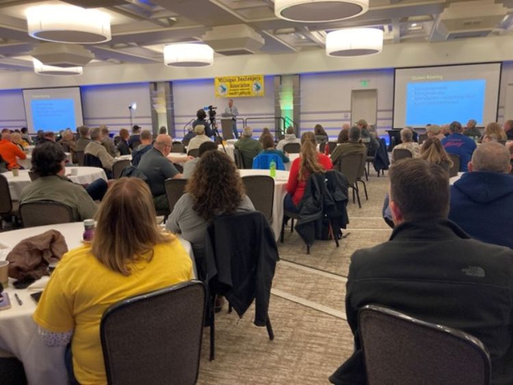 A room full of people siting and facing a presenter and a screen.