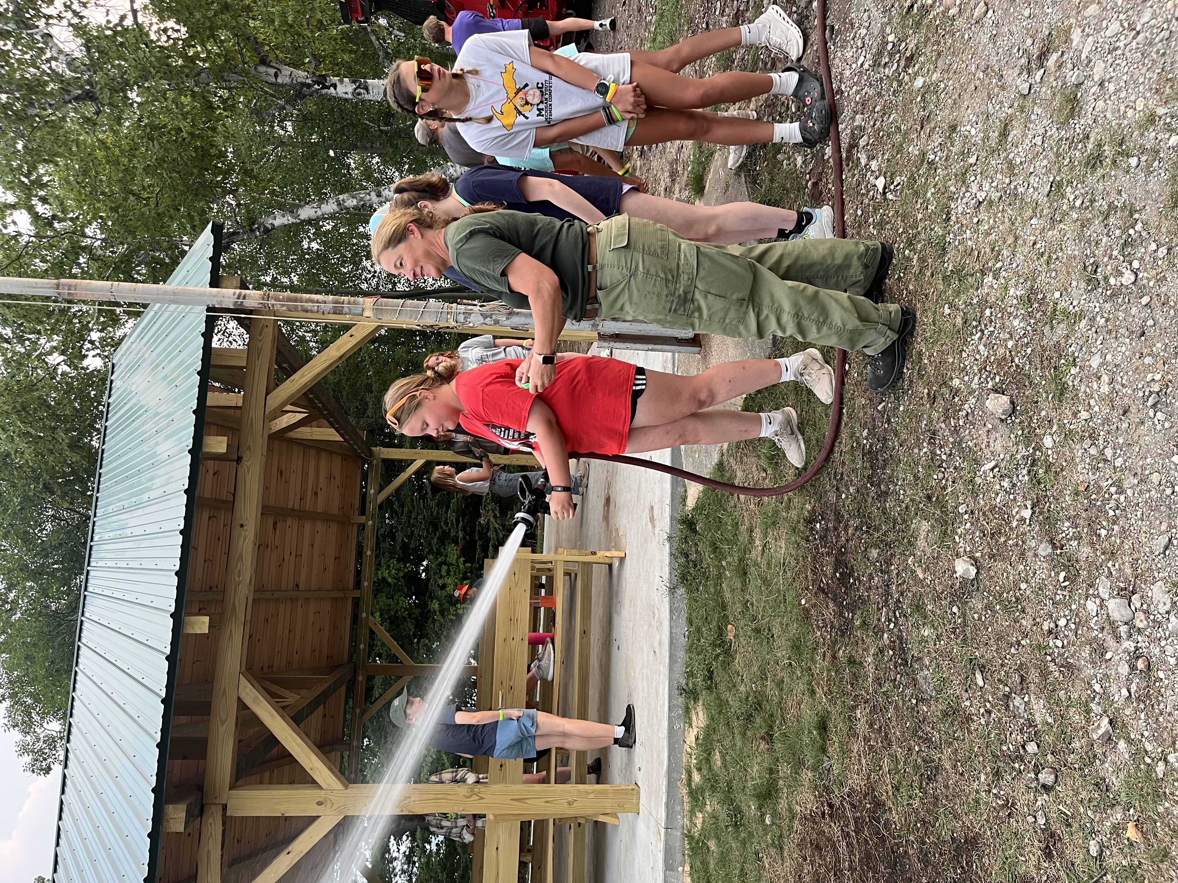 A firefighter teaches a camper how to handle the firehose.