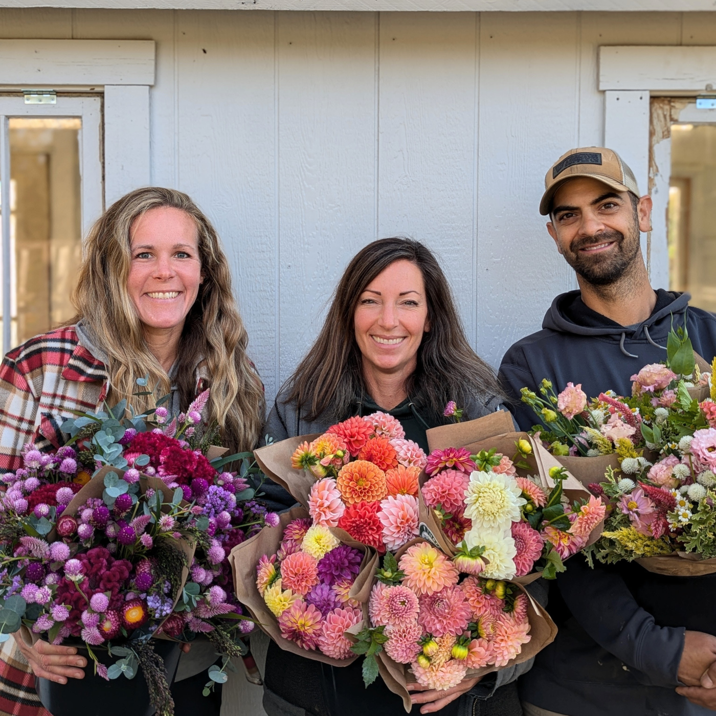 Three people pose for a picture holding bouquets of cut flowers.