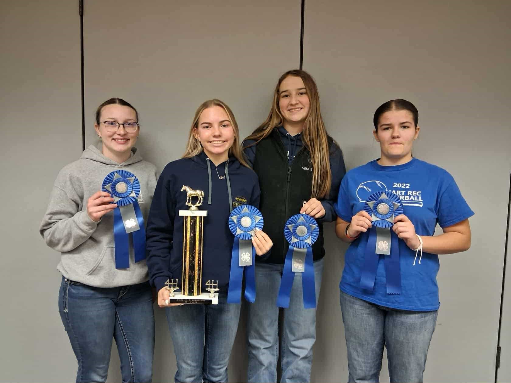 A group of young ladies holding up blue ribbons and a trophy.