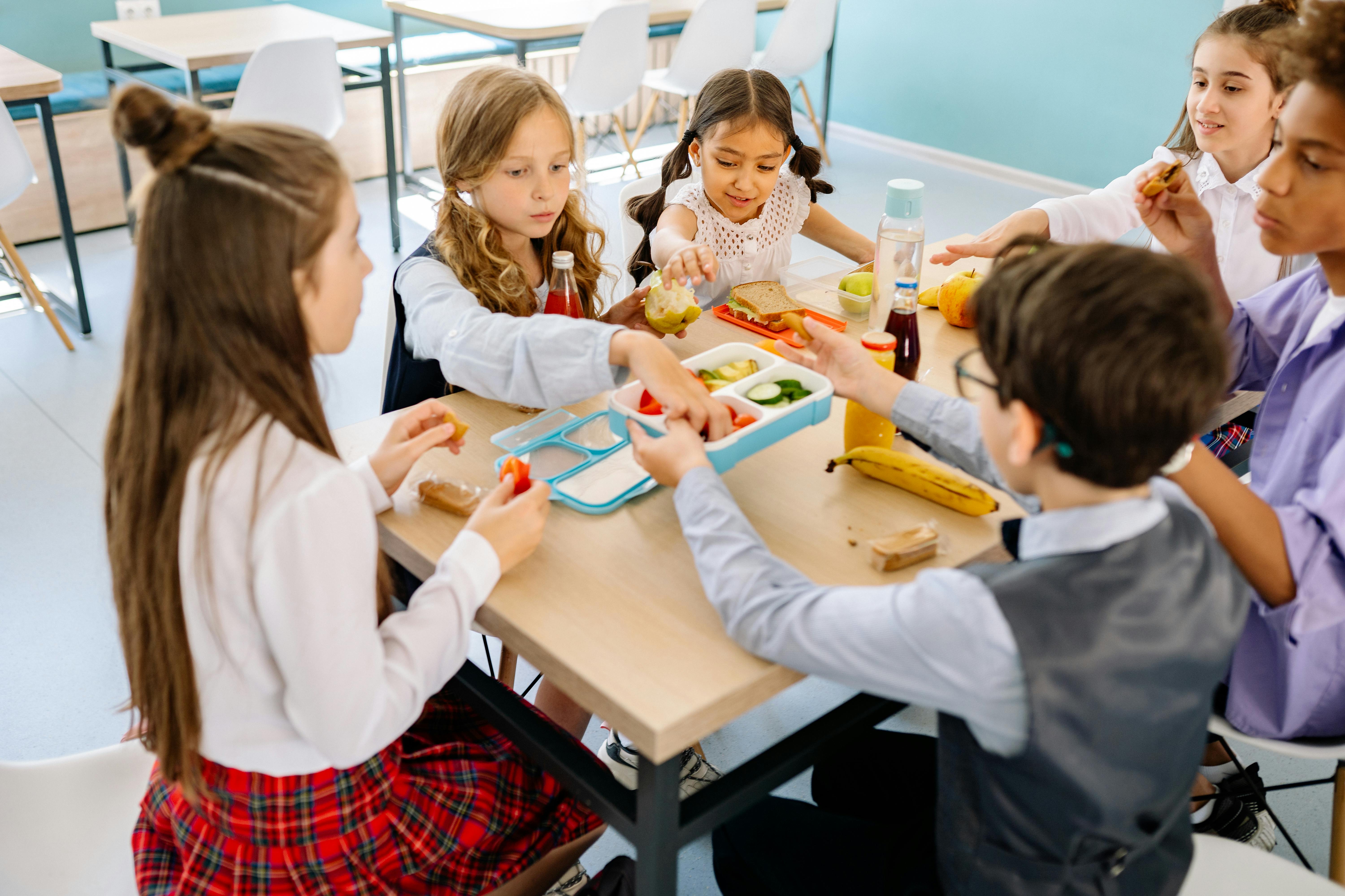 School children sitting around a table and sharing healthy lunch.